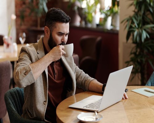 Person drinking coffee looking at a laptop screen